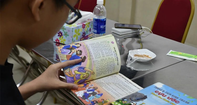 John lendo a Bíblia para crianças que está sendo distribuída no Vietnã
